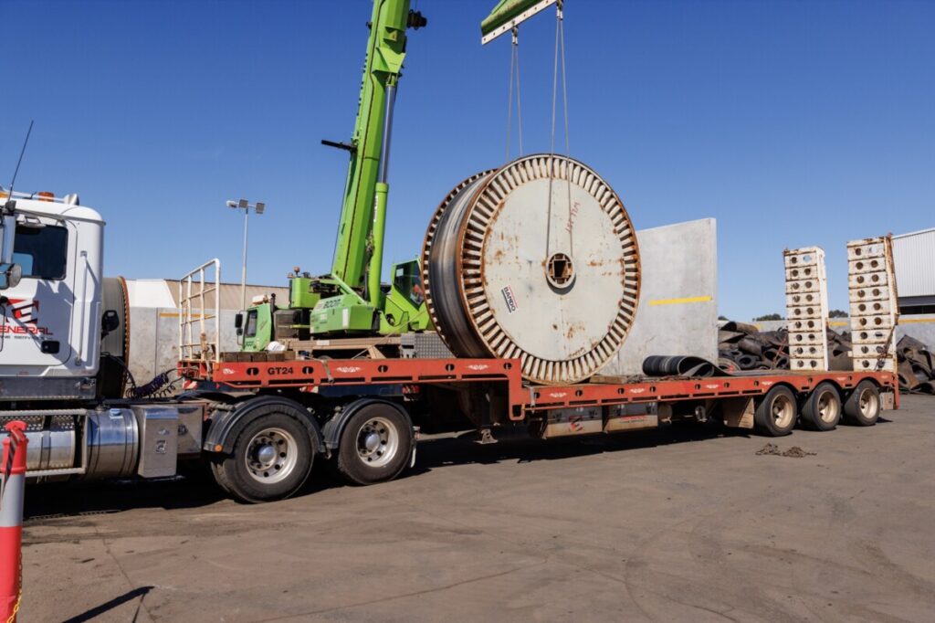 (Image source: Brodie Butler Photography) A crane prepares to unload one of 80 reels of used conveyer belt being sent from Alcoa’s mine sites to Tyrecycle in East Rockingham for recycling.